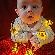 Léonie participe au concours pour gagner de l'argent avec cette photo : baby, blanket, child, closeup, cozy, curious_expression, cute, face, fairy_lights, glowing, hands, indoors, infant, portrait, red_background, soft_texture, toddler, warm_colors, warm_light, white_clothing