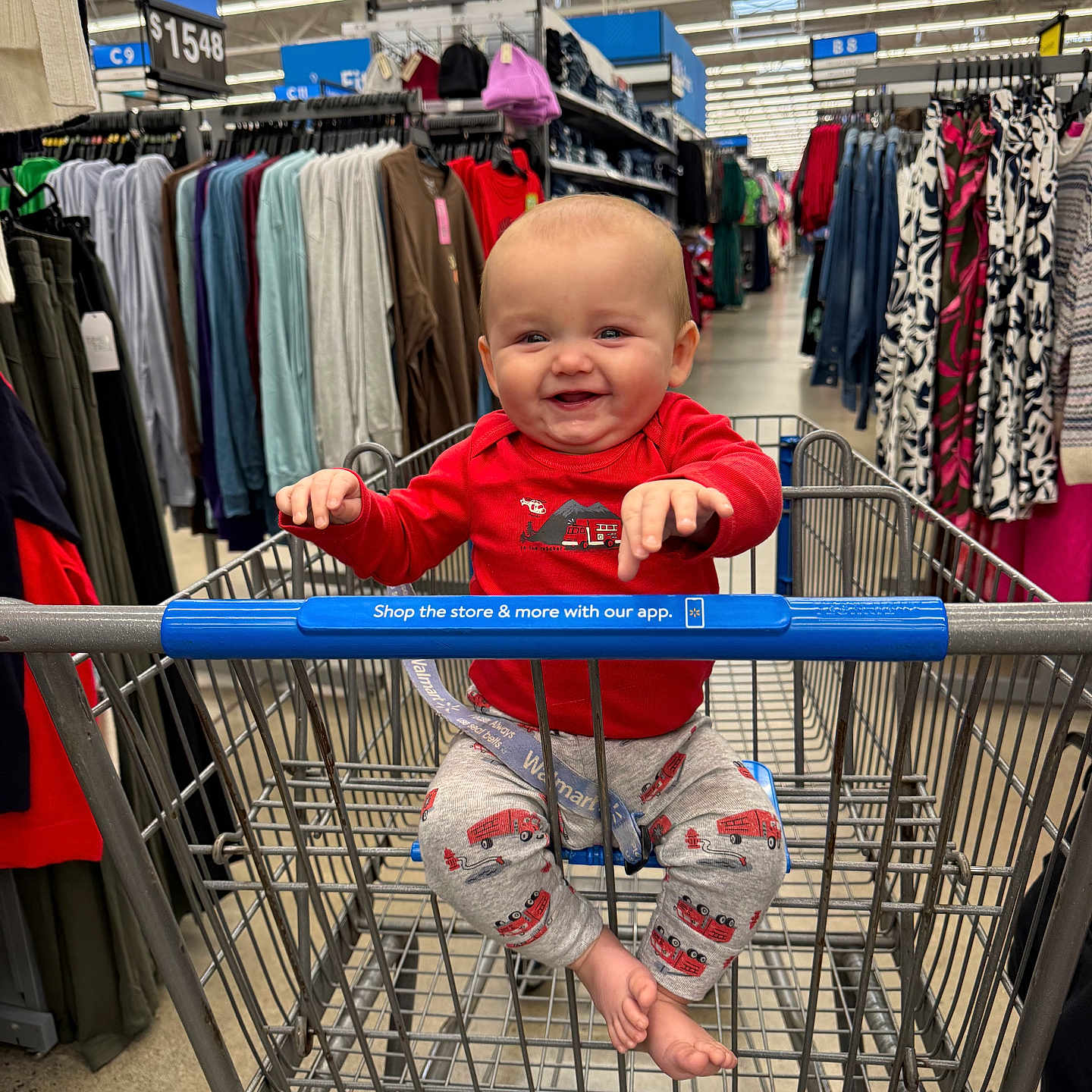 Bennett joined the competition — help win amazing prizes! aisle, baby, child, clothes, clothing_store, feet, fire_truck_pattern, hangers, happy, indoor, infant, metal_cart, pants, person, red_shirt, retail, shopping, shopping_cart, smiling, store_sign