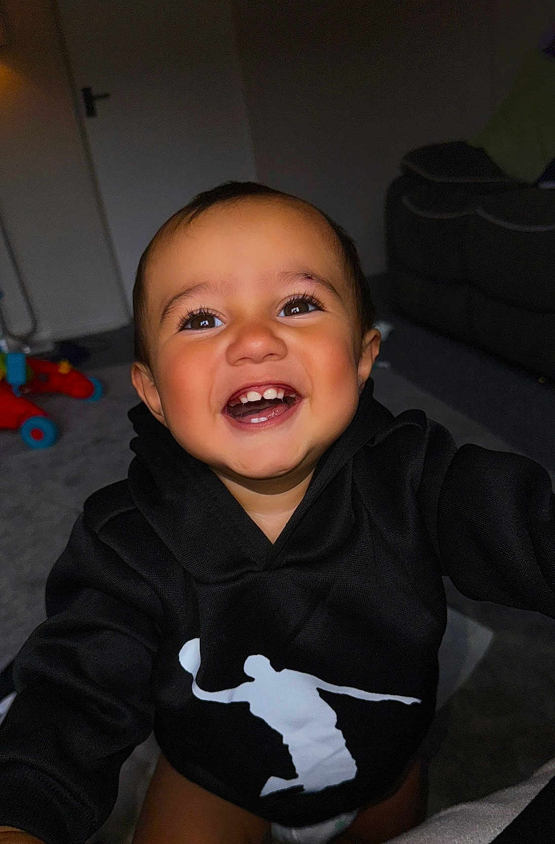 Lucas joined the competition — help win amazing prizes! toddler, child, smiling, happy, hoodie, indoor, face, teeth, black_clothing, toy, carpet, living_room, person, cute, joy, infant, baby, portrait, young_child, playful