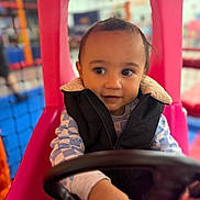 Lucas joined the competition — help win amazing prizes! black_jacket, blue_checkered_shirt, child, colorful, curious, cute, face, fun, hands, indoor, person, pink, play_area, playground_equipment, seat, smile, steering_wheel, toddler, toy_car, young_child