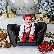 Thiago joined the competition — help win amazing prizes! baby, child, smiling, black_couch, red_plaid, hat, bowtie, teddy_bear, toy_truck, christmas_tree, christmas_decorations, wrapped_gifts, holiday, festive, indoor, portrait, happy, cute, seasonal, celebration