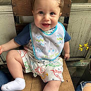 Andrez James joined the competition — help win amazing prizes! baby, child, smiling, bib, dinosaur_print, wooden_chair, drool, cute, happy, sitting, indoor, clothing, shorts, sock, person, portrait, hair, expression, yellow_flower, rustic_background