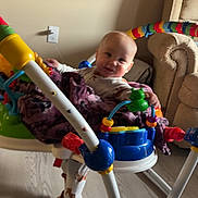 River is registered to the contest to win money with this photo: baby, blanket, activity_jumper, toy, colorful, indoor, floor, smiling, child, furniture, couch, playtime, cute, infant, happy, footwear, pajamas, wood_floor, person, home