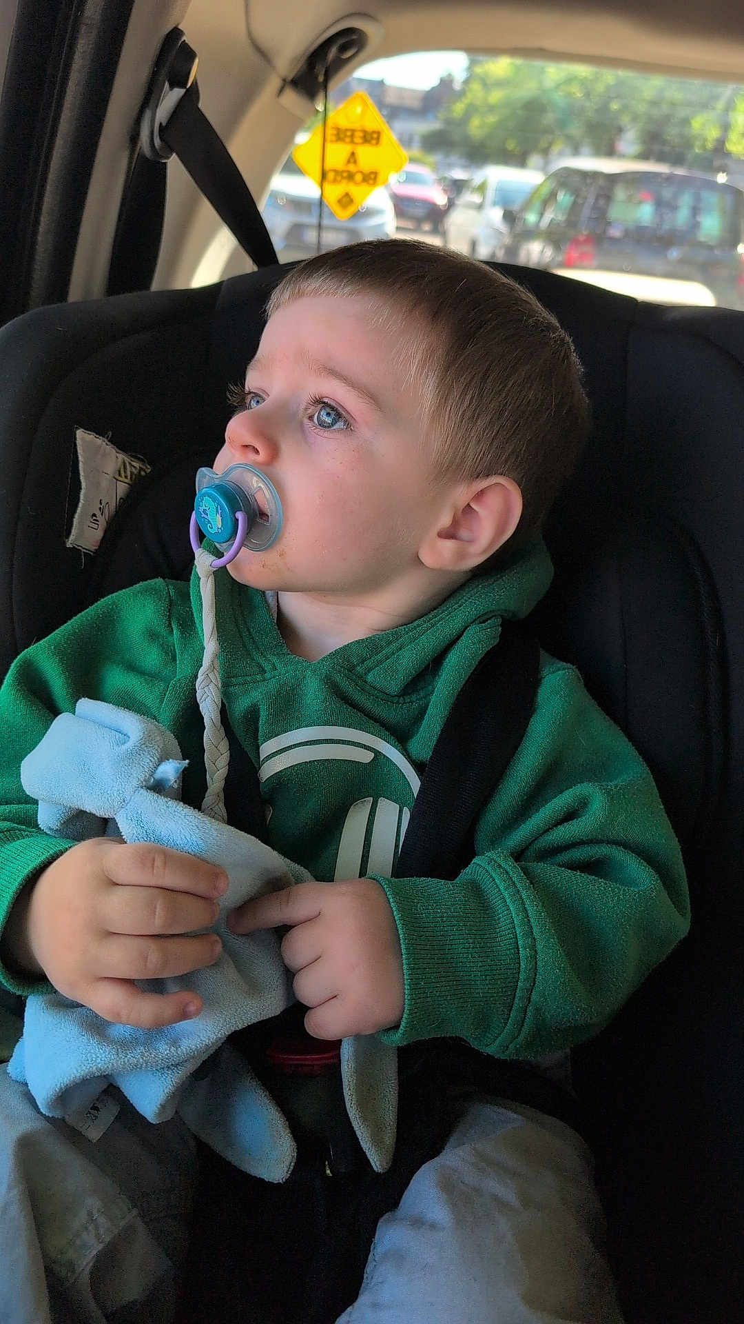 éren participe au concours pour gagner de l'argent avec cette photo : toddler, child, pacifier, green_hoodie, car_seat, blanket, blue_eyes, car_interior, seatbelt, window, daylight, clothing, hand, face, looking_away, young_child, casual_wear, transportation, safety, portrait