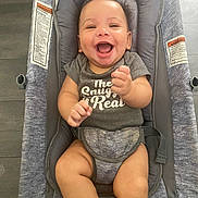 Brandon is registered to the contest to win money with this photo: baby, infant, smiling, laughing, onesie, baby_seat, cushion, gray, happy, child, indoors, floor, infant_clothing, cute, person, portrait, skin, seat_belt, baby_bouncer, sitting
