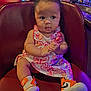 baby, child, sitting, dress, butterfly_pattern, sneakers, nike, orange, curly_hair, leather_chair, indoor, restaurant, bar, bottle, glass, person, cute, hands, expression, casual