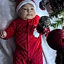 baby, infant, christmas, holiday, red_clothing, santa_hat, onesie, blanket, ornaments, decorations, festive, cute, chubby_cheeks, holiday_season, indoor, soft_texture, celebration, child, lying_down, curious