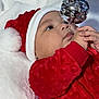 baby, infant, child, christmas, holiday, red_clothing, santa_hat, ornament, silver_ball, curious, festive, closeup, face, hands, soft_blanket, indoors, cute, winter, celebration, portrait