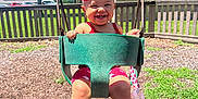 Normani is registered to the contest to win money with this photo: child, toddler, swing, playground, outdoor, smiling, happy, headband, red_clothing, shoes, socks, grass, trees, fence, sunny, daytime, baby, park, fun, play