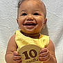 Normani is registered to the contest to win money with this photo: baby, child, smile, yellow_dress, earrings, wooden_plaque, 10_months, portrait, happy, infant, closeup, cute, hands, face, indoor, sitting, young_child, celebration, bright, texture