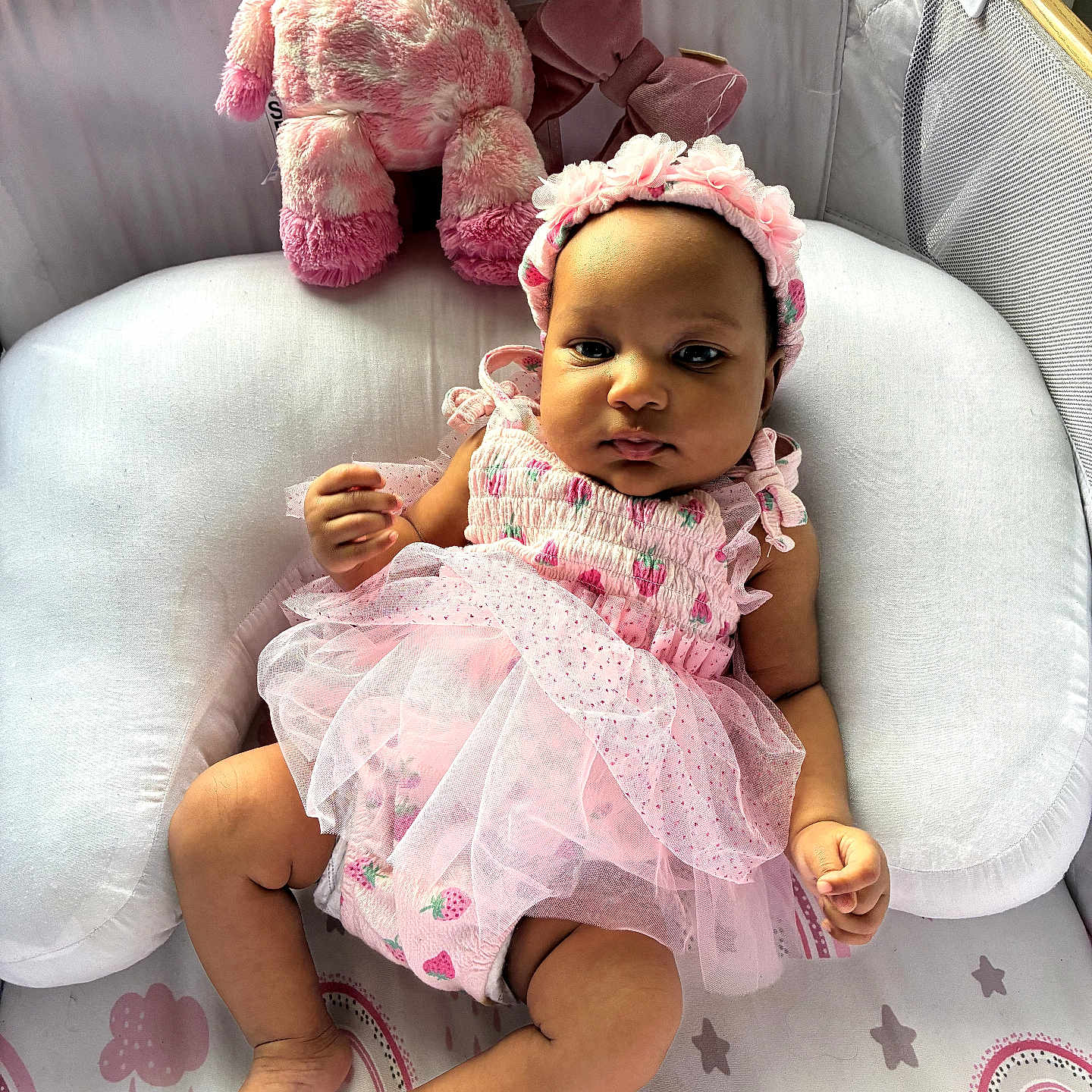 Stevie joined the competition — help win amazing prizes! baby, infant, pink_dress, headband, plush_toy, stuffed_giraffe, cushion, nursery, patterned_bedding, rainbow, stars, soft_toys, child, indoors, portrait, cute, toddler, clothing, relaxing, smiling
