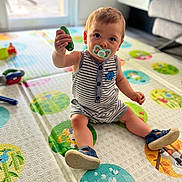 Louis participe au concours pour gagner de l'argent avec cette photo : toddler, child, indoor, playmat, toy, pacifier, striped_clothing, footwear, sitting, curious, colorful, floor, living_room, window, carpet, person, young_child, cute, baby, home