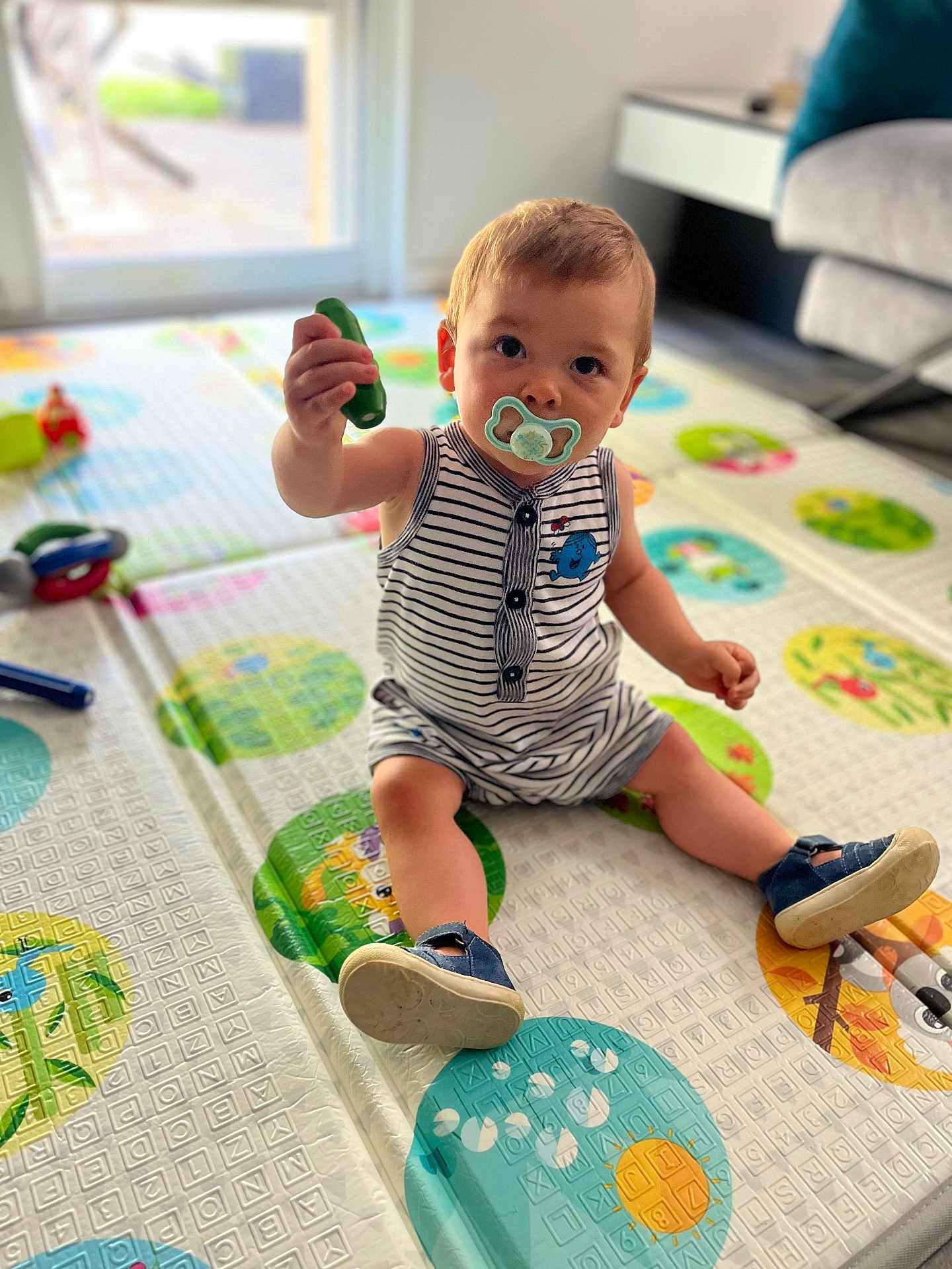 Louis participe au concours pour gagner de l'argent avec cette photo : toddler, child, indoor, playmat, toy, pacifier, striped_clothing, footwear, sitting, curious, colorful, floor, living_room, window, carpet, person, young_child, cute, baby, home