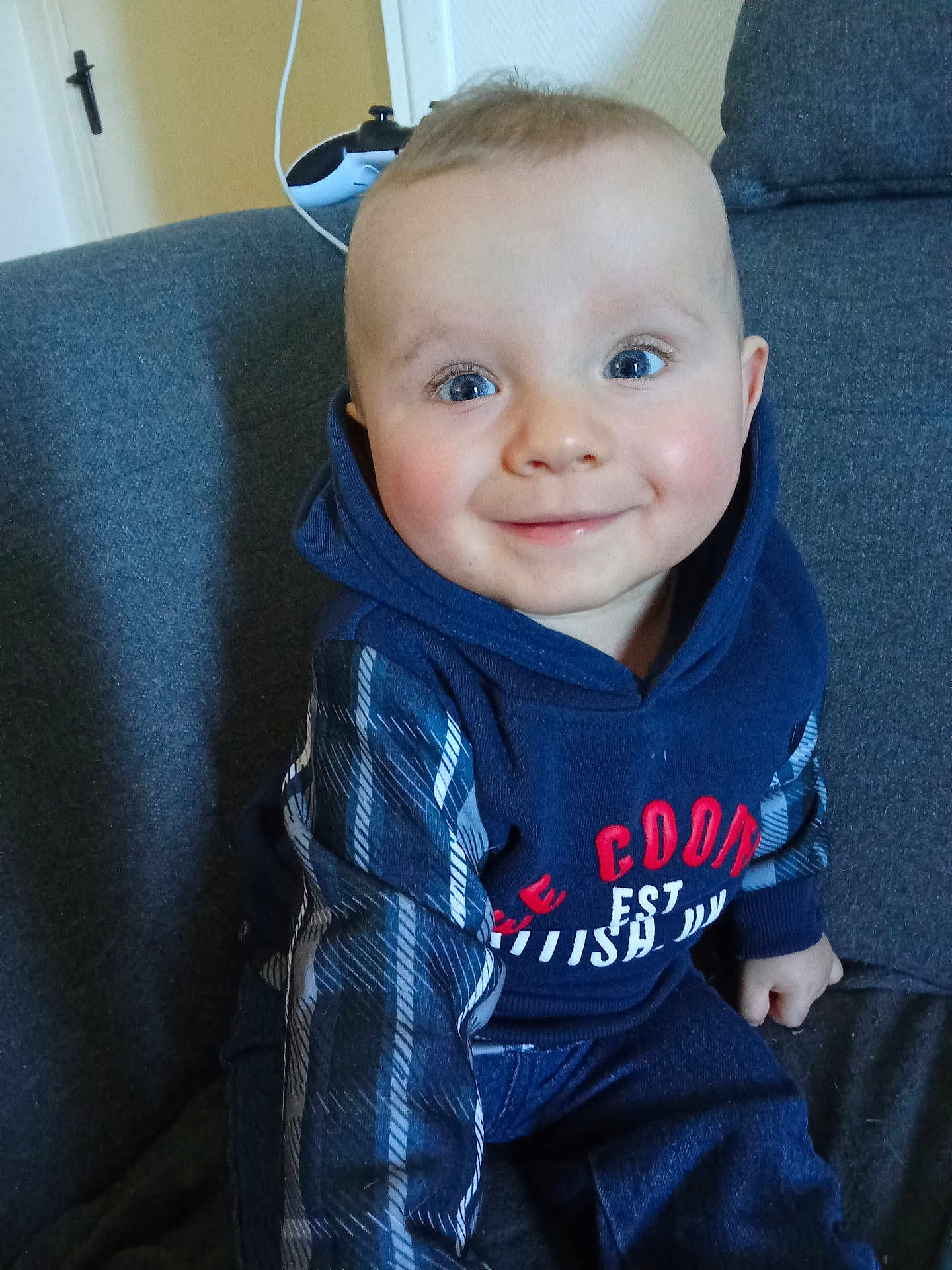 Juliann a rejoint le concours — aidez-le/la à gagner de superbes lots ! baby, child, smiling, blue_eyes, hoodie, plaid, sitting, couch, indoor, happy, person, cute, young, face, clothing, portrait, infant, rosy_cheeks, casual, comfort