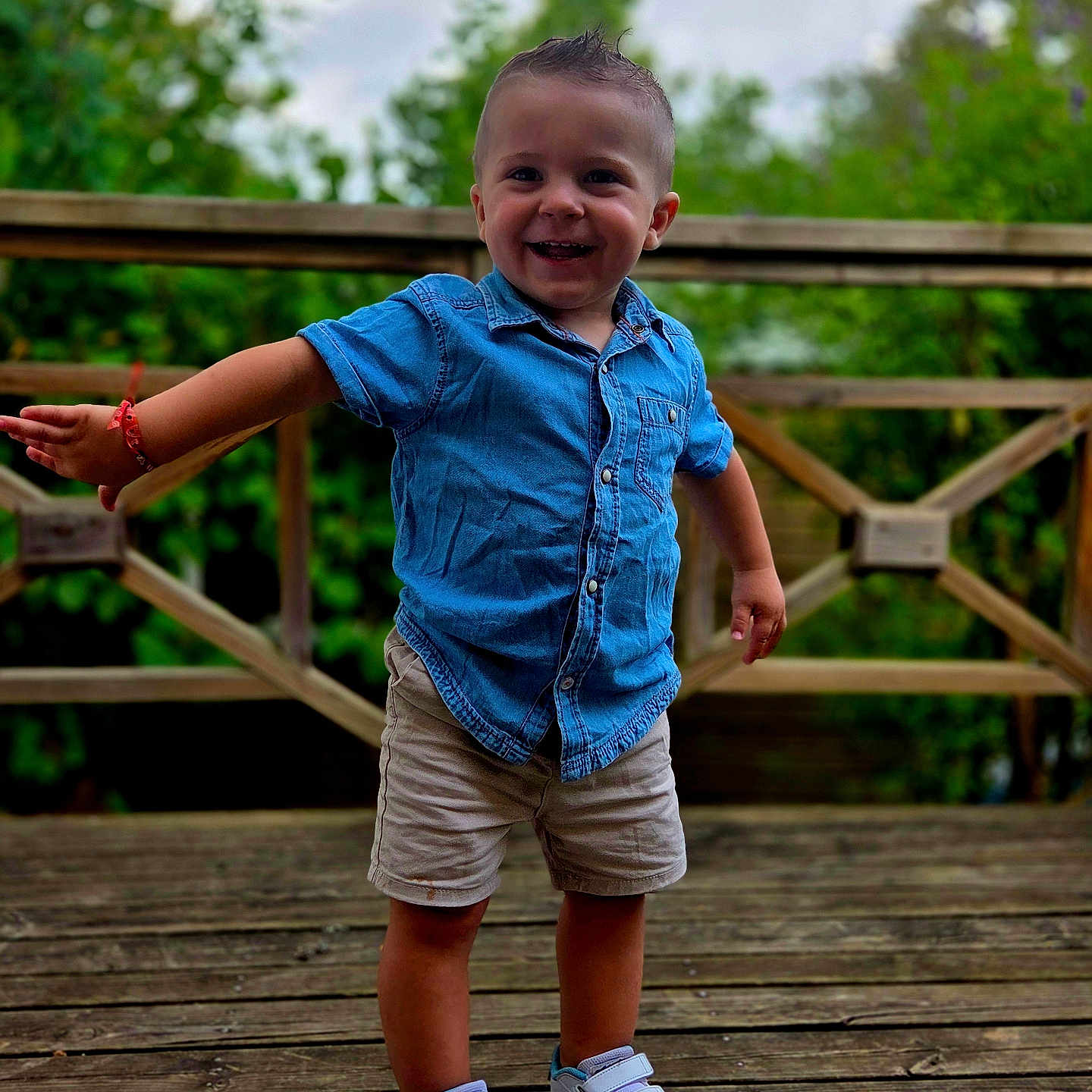 Maël participe au concours pour gagner de l'argent avec cette photo : boy, bracelet, casual_clothing, child, daytime, denim_shirt, feet, greenery, happy, natural_light, outdoor, playful, portrait, short_hair, shorts, smiling, sneakers, standing, toddler, wooden_deck