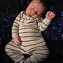baby, sleeping, pajamas, striped_clothing, infant, blanket, dark_background, cosmic_pattern, hand, footwear, sock, cute, peaceful, portrait, resting, child, soft_texture, indoor, cozy, newborn