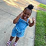 child, toddler, denim_outfit, purple_sandals, sidewalk, grass, peace_sign, tongue_out, playful, outdoor, sunlight, happy, cute, portrait, summer, person, hair_puff, casual_clothing, fun, smiling