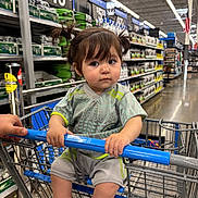 Isabella joined the competition — help win amazing prizes! toddler, child, shopping_cart, store, aisle, shelves, products, clothing, pigtails, hair, hands, floor, retail, shopping, person, indoor, expression, grip, blue, casual