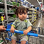toddler, child, shopping_cart, store, aisle, shelves, products, clothing, pigtails, hair, hands, floor, retail, shopping, person, indoor, expression, grip, blue, casual