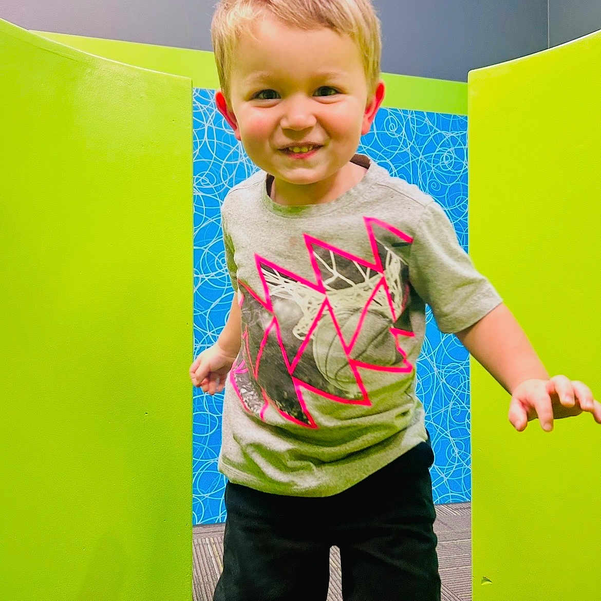 Ridikk joined the competition — help win amazing prizes! blue_wall, boy, bright, carpeted_floor, casual_clothing, child, colorful_background, cute, fun, green_panels, happy, indoor, person, playful, portrait, short_hair, shorts, smiling, tshirt, young