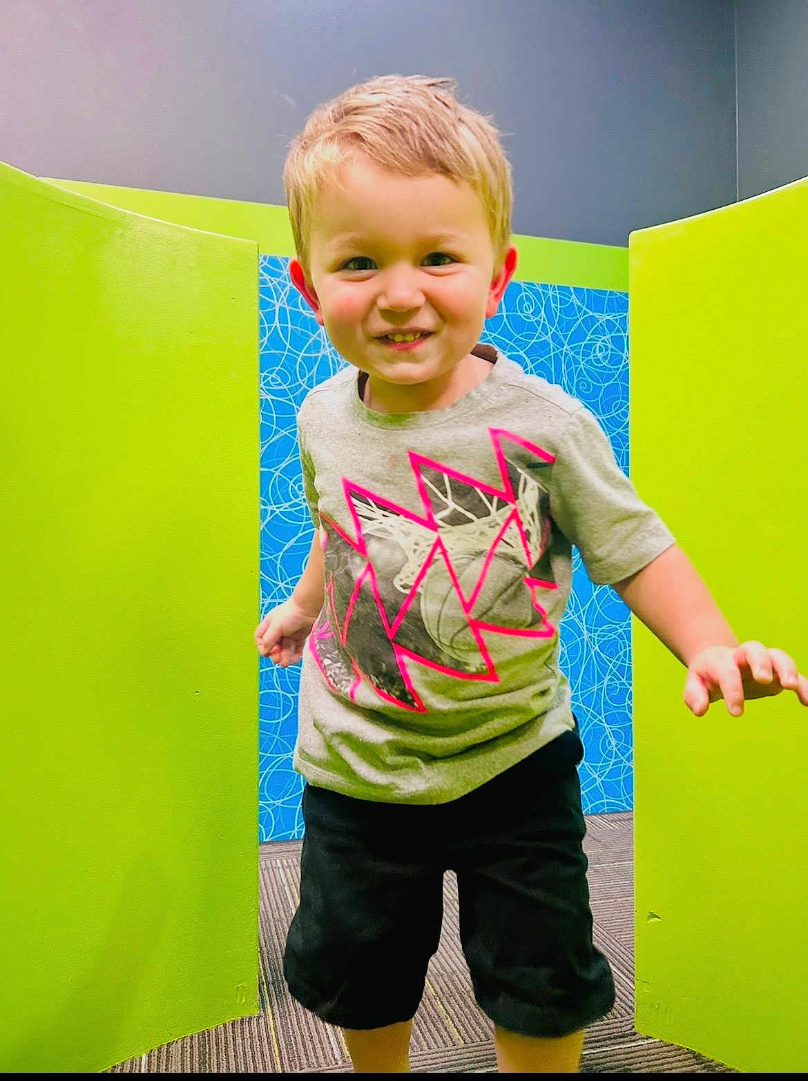 Ridikk joined the competition — help win amazing prizes! child, boy, smiling, shorts, tshirt, indoor, colorful_background, green_panels, blue_wall, carpeted_floor, playful, portrait, happy, cute, person, young, casual_clothing, short_hair, bright, fun