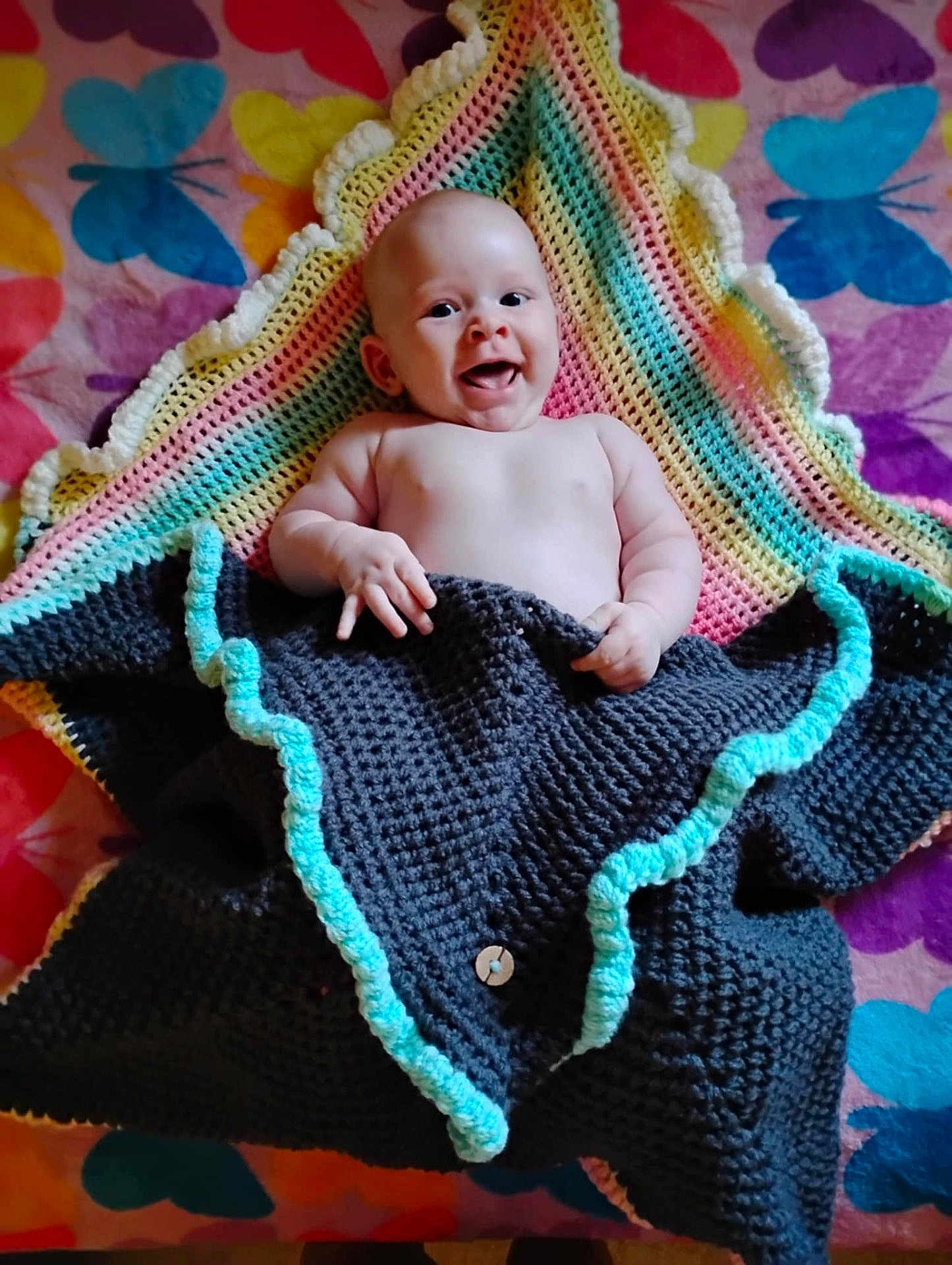 Willow joined the competition — help win amazing prizes! baby, smiling, blanket, crocheted_blanket, colorful, butterfly_pattern, happy, infant, child, lying_down, cozy, hand, face, skin, indoor, cute, young_child, textile, pattern, warm
