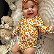 Arya participe au concours pour gagner de l'argent avec cette photo : baby, smiling, infant, headband, onesie, leopard_print, stuffed_animal, blanket, soft_toy, cushion, happy, cute, child, indoor, portrait, cozy, plush, lying_down, face, adorable