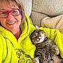 woman, cat, glasses, hoodie, grinch, couch, blanket, smiling, happy, cozy, indoor, tabby_cat, pet, relaxed, sleepy, furniture, portrait, casual, comfort, friendship