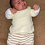 baby, brown_background, casual, child, clothing, cozy, cream_top, cute, expression, fist, indoors, infant, lying_down, newborn, person, portrait, small_hands, socks, soft_texture, striped_pants
