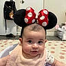 baby, infant, headband, minnie_mouse, bow, polka_dot, bib, baby_seat, indoor, carpet, door, bag, floor, cute, child, person, face, expression, clothing, home