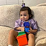Alexus joined the competition — help win amazing prizes! toddler, child, toy, stacking_toy, purple_shirt, bow, couch, beige, indoor, smiling, cute, play, socks, hair, face, person, home, furniture, relaxed, colorful