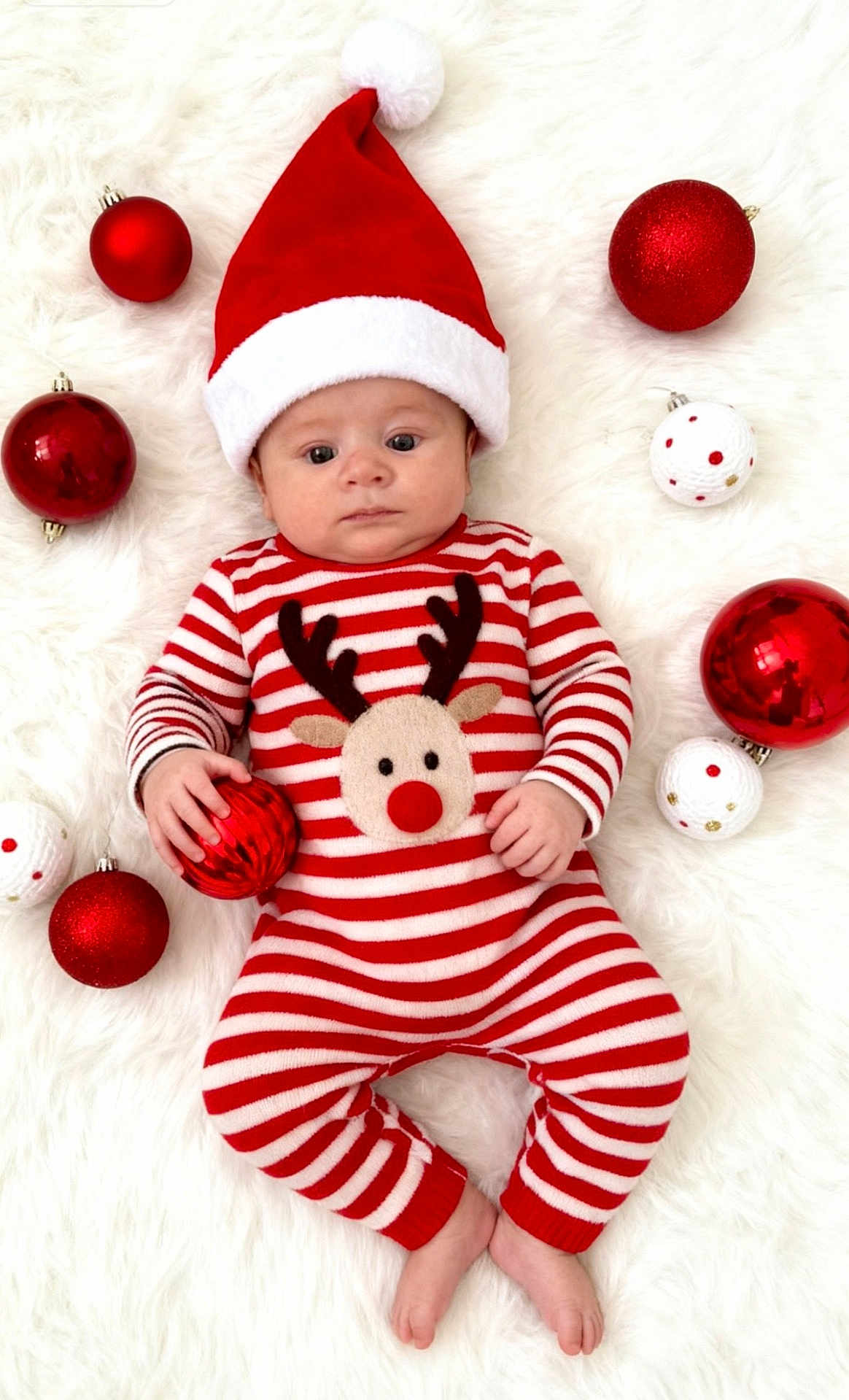 Lennie-Roy joined the competition — help win amazing prizes! baby, christmas, festive, santa_hat, red_and_white, striped_onesie, reindeer, ornaments, red_baubles, white_baubles, fluffy_background, holiday, cute, infant, lying_down, holding_object, celebration, seasonal, soft_texture, portrait