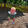 Kohen is registered to the contest to win money with this photo: baby, child, clothing, fence, greenery, happy, outdoor, park, person, playground, shadow, shorts, smiling, socks, summer, sunlight, swing, toddler, tree, wood_chips