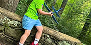 Liam is registered to the contest to win money with this photo: child, boy, toy_airplane, green_shirt, red_shoes, white_socks, stone_wall, forest, trees, nature, outdoor, play, smile, happy, casual_clothing, summer, daylight, young, person, leaves