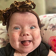 Adalynn is registered to the contest to win money with this photo: baby, infant, smiling, tongue_out, headband, brown_headband, blue_eyes, cheeks, black_clothing, floral_pillow, closeup, face, happy, cute, child, skin, indoors, person, portrait, expression