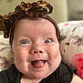 baby, infant, smiling, tongue_out, headband, brown_headband, blue_eyes, cheeks, black_clothing, floral_pillow, closeup, face, happy, cute, child, skin, indoors, person, portrait, expression