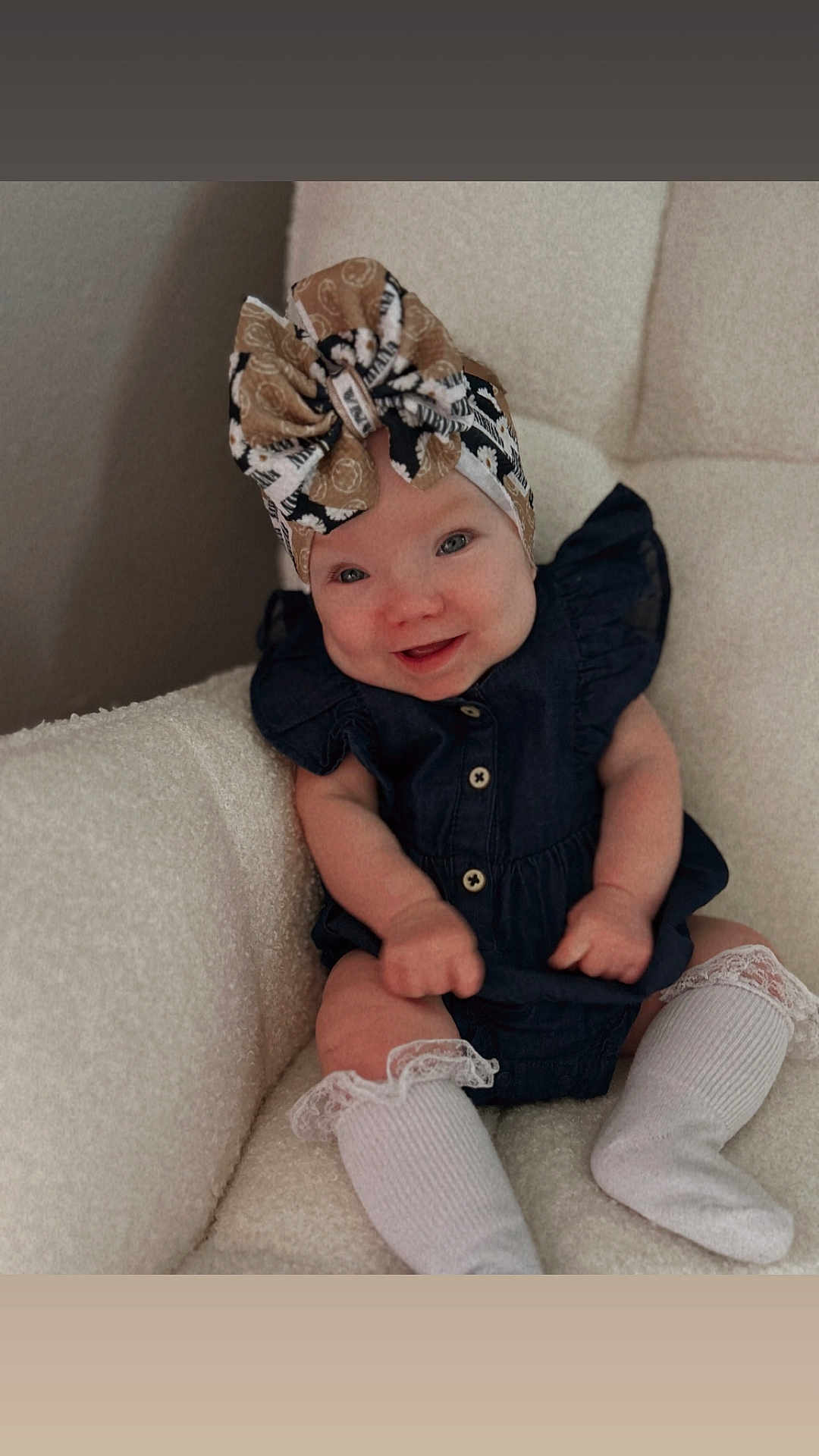 Adalynn is registered to the contest to win money with this photo: baby, child, smiling, headwrap, dress, socks, white, dark_clothing, sitting, chair, indoor, plush, cute, happy, infant, person, portrait, cozy, fashion, comfortable