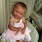 Azalea is registered to the contest to win money with this photo: baby, child, smiling, tutu, pink_dress, car_seat, beige_leather, happy, cute, portrait, sitting, person, infant, curly_hair, barefoot, holding_object, closeup, indoor, seatbelt, car_interior