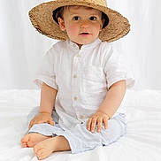 Marcus a rejoint le concours — aidez-le/la à gagner de superbes lots ! toddler, child, hat, straw_hat, white_shirt, pants, barefoot, indoor, bed, white_bedspread, cute, portrait, sitting, curious, face, hands, feet, baby, casual_clothing, soft_lighting