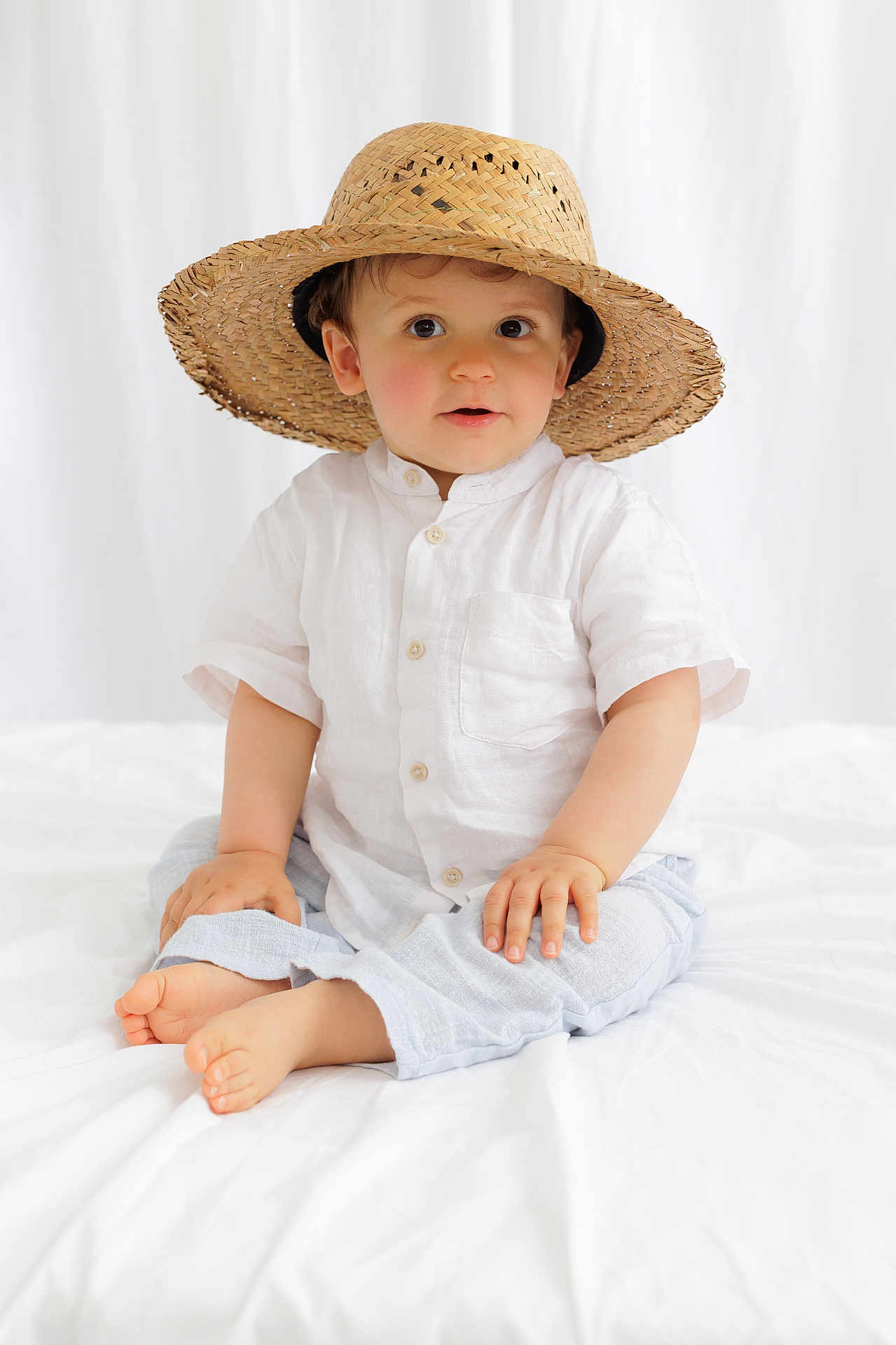 Marcus a rejoint le concours — aidez-le/la à gagner de superbes lots ! toddler, child, hat, straw_hat, white_shirt, pants, barefoot, indoor, bed, white_bedspread, cute, portrait, sitting, curious, face, hands, feet, baby, casual_clothing, soft_lighting