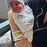 newborn, baby, swaddled, bow_hat, rainbow_pattern, tattoo, adult, nails, pink_nails, hospital_bracelet, window, daylight, indoor, seated, woman, holding_baby, black_clothing, comfort, cute, portrait