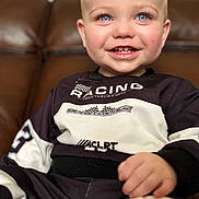Harry is registered to the contest to win money with this photo: toddler, child, smiling, blue_eyes, racing_outfit, sitting, couch, leather, happy, portrait, indoor, clothing, cute, baby, person, young_child, face, hand, casual, closeup