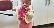 A'Yari joined the competition — help win amazing prizes! toddler, child, indoor, standing, pink_clothing, jacket, shoes, wooden_floor, cabinet, chair, curly_hair, bracelet, expression, furniture, support, young_child, person, flooring, holding, casual_wear