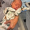 newborn, baby, infant, sleeping, portrait, person, holding, cradled, onesie, dinosaur_print, clothing, kitchen, countertop, cabinets, stove, granite, home, indoor, caregiver, cozy