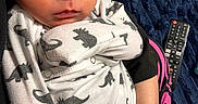 Augustine joined the competition — help win amazing prizes! newborn, baby, infant, child, face, eyes, portrait, lying_down, dinosaur_pajamas, onesie, clothing, blanket, navy_blue, remote_control, adult_hand, indoor, cozy, cute, home, close_up