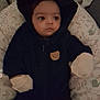 baby, infant, hoodie, bear_patch, gloves, cushion, patterned_bedding, indoor, child, portrait, face, eyes, cute, cozy, soft, clothing, lying_down, warm, expression, young