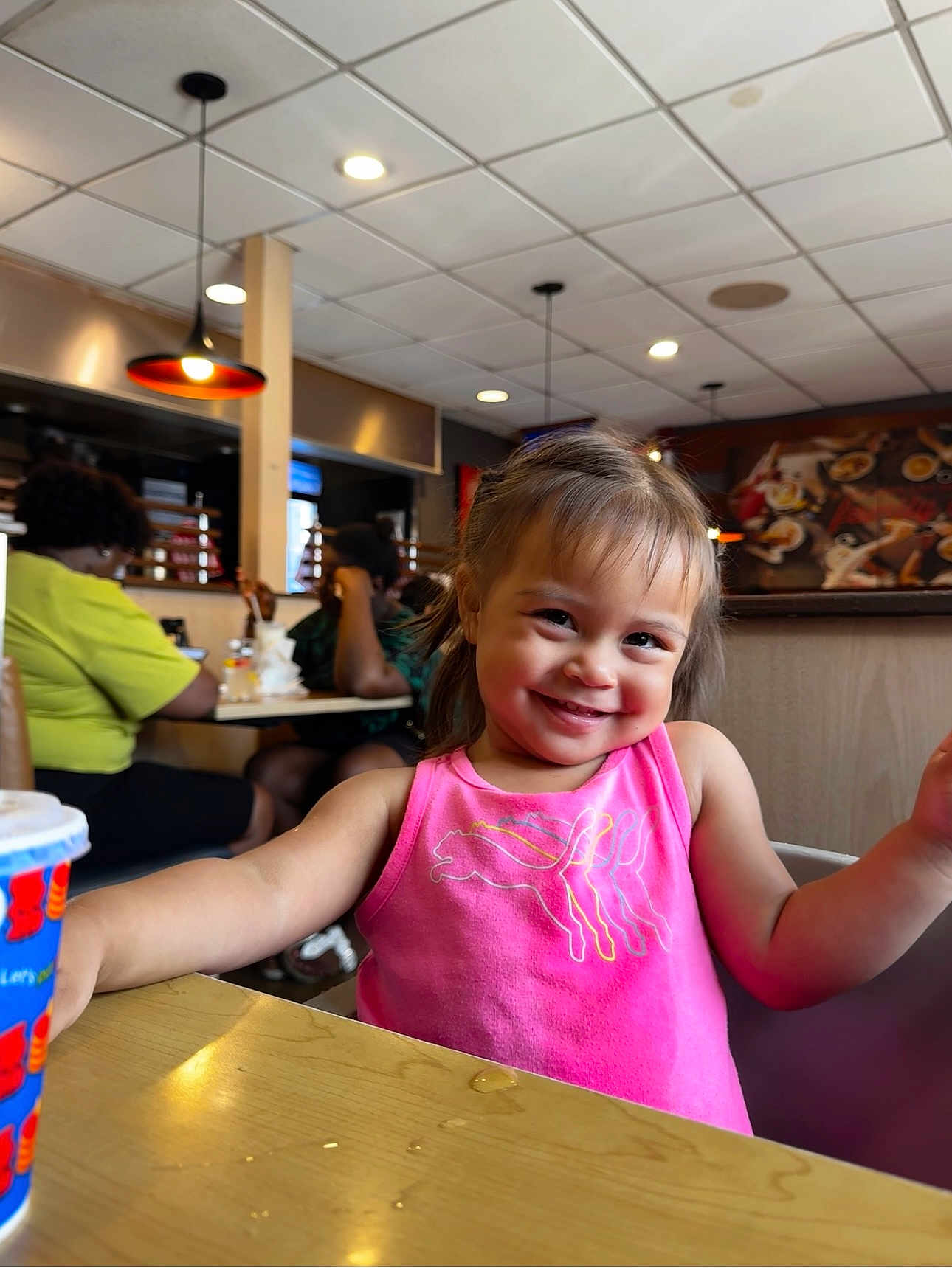 Aylani joined the competition — help win amazing prizes! toddler, child, smile, pink_shirt, restaurant, table, cup, indoor, people, background, happy, face, hairstyle, seat, lighting, casual, dining, fun, person, portrait
