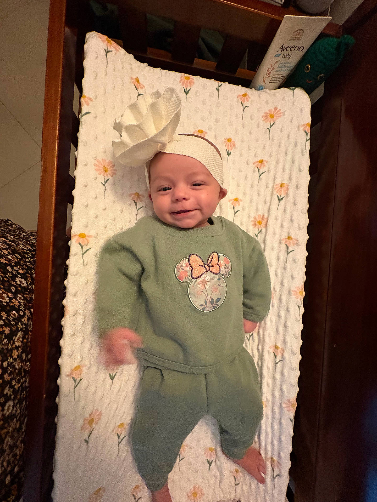 Emma joined the competition — help win amazing prizes! baby, blanket, child, crib, cute, face, floral_pattern, flower, foot, green_clothing, happy, headband, indoors, infant, laying_down, person, portrait, smiling, toddler, wooden_furniture