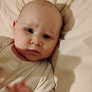 Scottie is registered to the contest to win money with this photo: baby, infant, face, hand, blanket, pajamas, soft, curious, closeup, expression, skin, head, lying_down, indoors, child, human, portrait, sleepwear, comfort, young