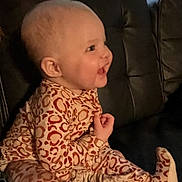 Nova is registered to the contest to win money with this photo: baby, child, smiling, leopard_print, onesie, clothing, sitting, couch, leather, indoor, face, head, person, happy, window, background, pattern, infant, cute, portrait